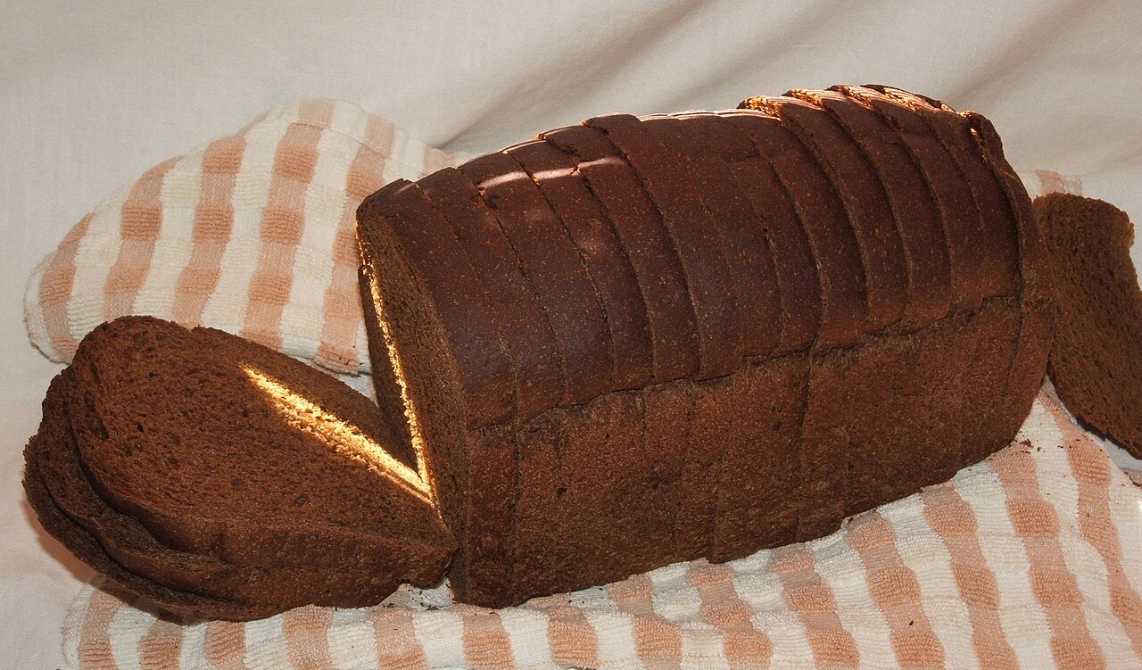 A sliced loaf of dark rye bread on a striped kitchen towel